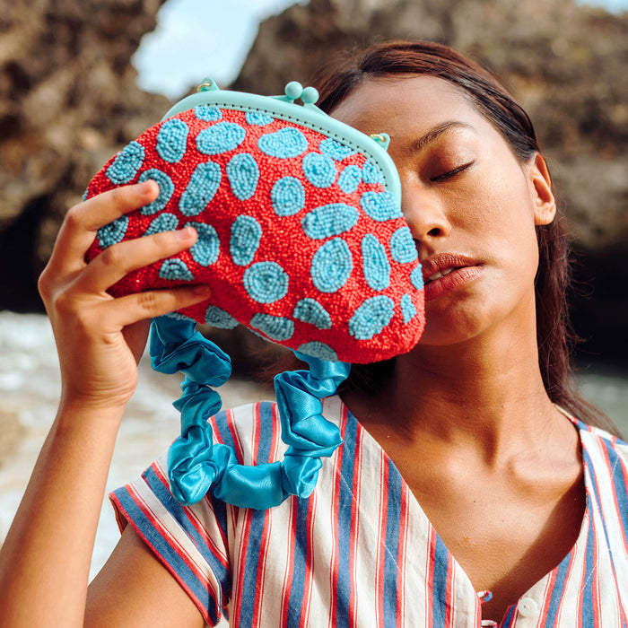 BrunnaCo Arnoldi Ariela Handbeaded clutch in red and turquoise blue color is an artisanal handmade piece by female artisans in Bali. This handbag clutch is carefully and sustainably made using glass beads in playful polka dot pattern.