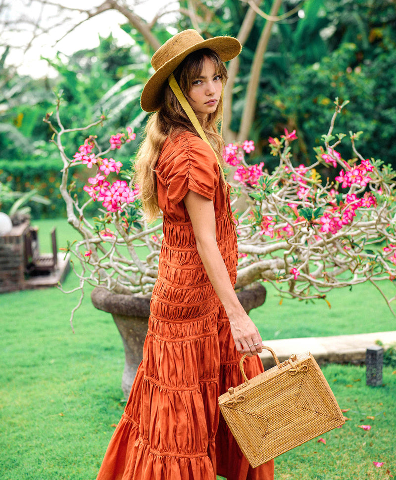 Inka Williams is holding BrunnaCo's Rahayu Atta Rattan Bag handmade in Bali using natural Atta rattan straws from Lombok. Inka is wearing BrunnaCo's Srikandi Ruffle Christmas dress in Sienna Brown. Designed in California.