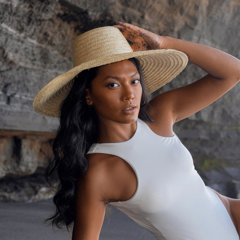 A woman is wearing BrunnaCo Rianna Straw hat made from locally harvested palm straw in Bali. This versatila hat is perfect for a day at the beach or a stroll around town on a sunny summer day