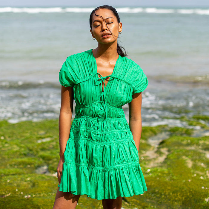 A woman is wearing SRIKANDI Ruffle Cotton Dress In Kelly Green at the tropical beach in Cannes, France Bingin Bali