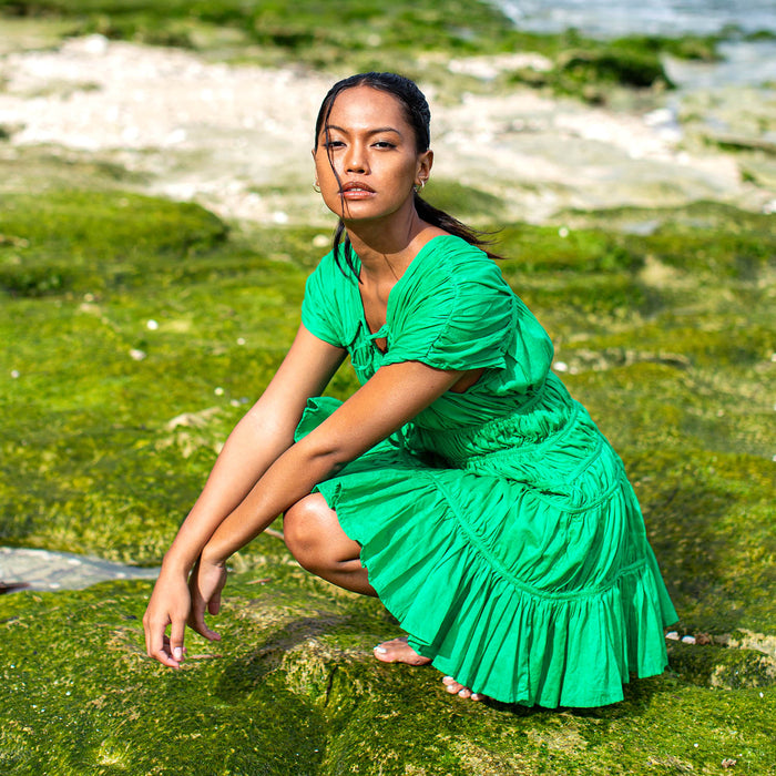 A woman is wearing SRIKANDI Ruffle Cotton Dress In Kelly Green at the tropical beach in Cannes, France Bingin Bali