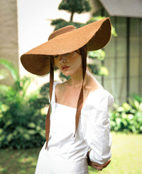 Lola Wide Brim Jute Straw Hat In Havana Brown. Braided meticulously by artisans in Gianyar, Bali from natural Jute material, this sweet hat offers both comfort and elegance. Designed with ideal thickness and weight that allow its brim to be easily folded, stretched, and styled, making it easy to take to any holiday trips or summer vacation.