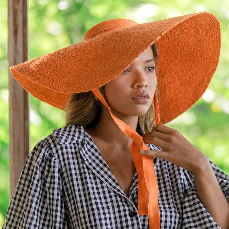 LOLA Wide Brim Jute Straw Hat In Orange. Braided meticulously by artisans in Gianyar, Bali from natural Jute material, this sweet hat offers both comfort and elegance. Designed with ideal thickness and weight that allow its brim to be easily folded, stretched, and styled, making it easy to take to any holiday trips or summer vacation.