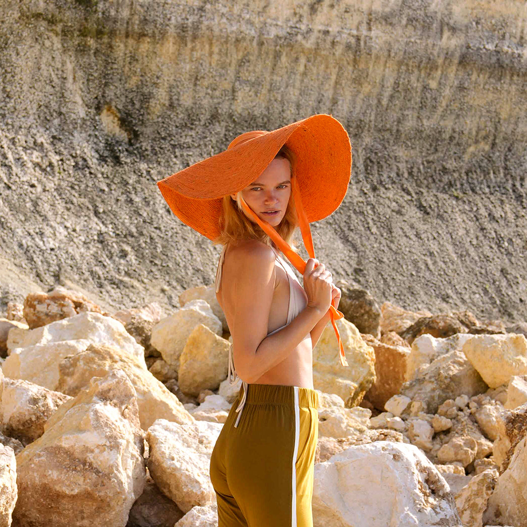 LOLA Wide Brim Jute Straw Hat In Orange. Braided meticulously by artisans in Gianyar, Bali from natural Jute material, this sweet hat offers both comfort and elegance. Designed with ideal thickness and weight that allow its brim to be easily folded, stretched, and styled, making it easy to take to any holiday trips or summer vacation.