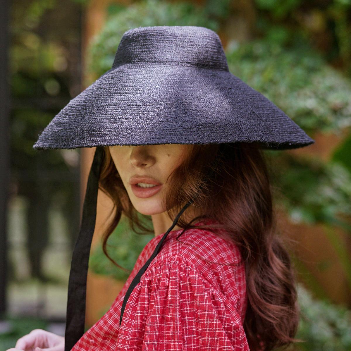 A woman is wearing BrunnaCo Reign Jute Straw hat for a summer stroll at the beach. The hat is sustainable and made by artisans in Bali