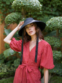 A woman is wearing BrunnaCo Reign Jute Straw hat for a summer stroll at the beach. The hat is sustainable, vegan, and made by artisans in Bali